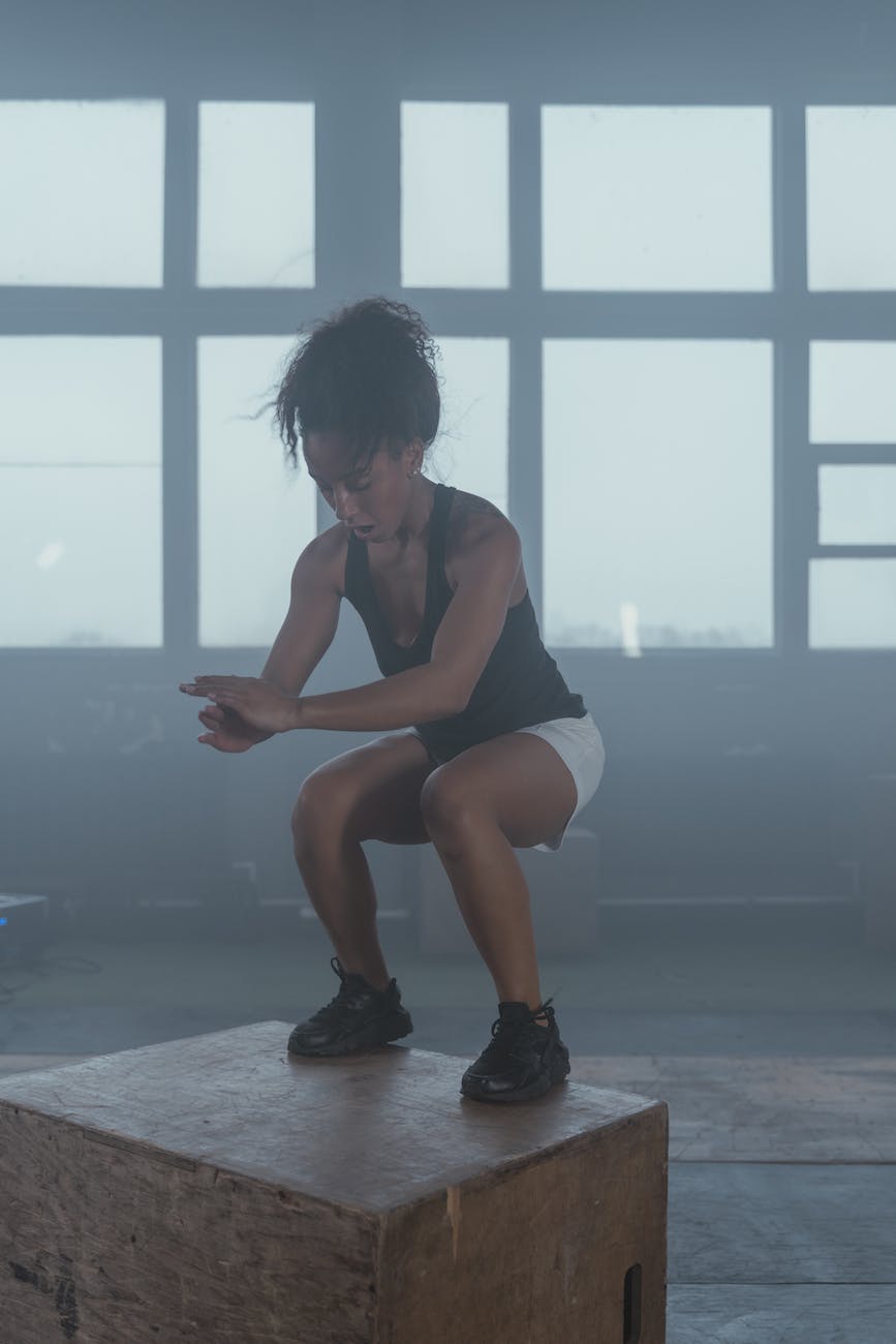 a woman in black tank top doing squats on a wooden block