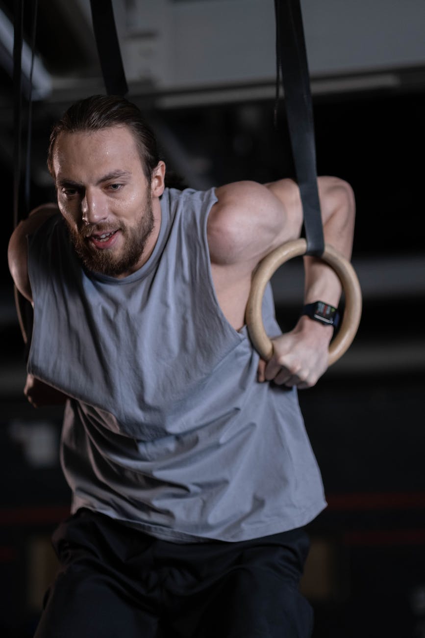 man in gray tank top holding onto gymnastic rings